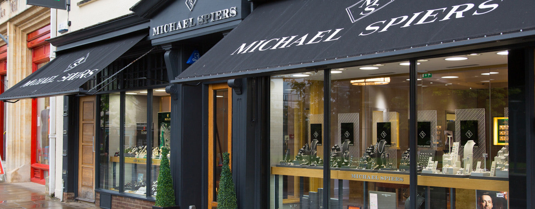 A black awning on Michael Spiers jewellers Exeter storefront in Exeter city centre on Cathedral Green. Exquisite jewellery brands are on display including necklaces, rings, earrings, bracelets and fine watches from Omega, Tag Heuer, Gucci, Tissot, Fope, Georg Jensen. 