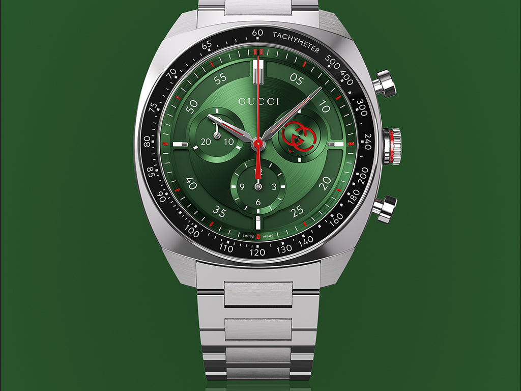 A silver Gucci wristwatch with a green dial and chronograph features, displayed against a green background.