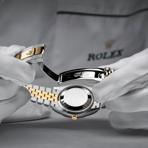 A man in a white Rolex jacket is carefully inspecting a Rolex watch during a service.
