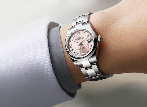 Rolex DateJust watch with a pink face on a woman's write. Her lilac suit cuff is visible.
