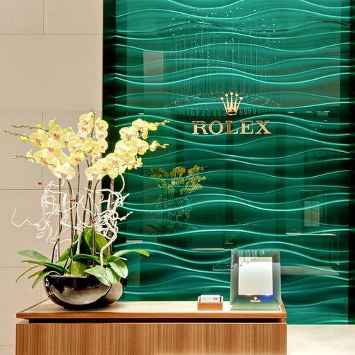 The Rolex reception desk at a Michael Spiers desk. Beautiful yellow flowers sit on the desk with the Rolex logo seen on the wall behind the desk.