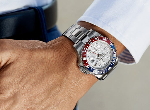 A mens Rolex GMT Master watch being worn by a man in a light blue shirt.