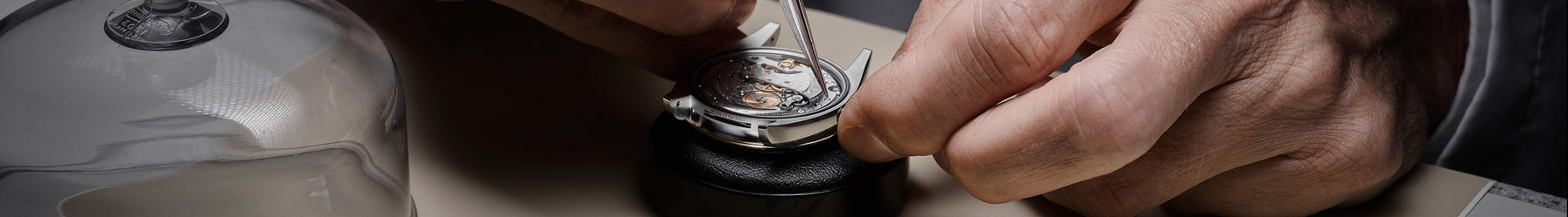 A man is delicately servicing a Rolex using a pair of tweezers.