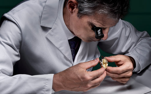 A man in a white jacket carefully inspects the inner workings of a Rolex watch during a Rolex service