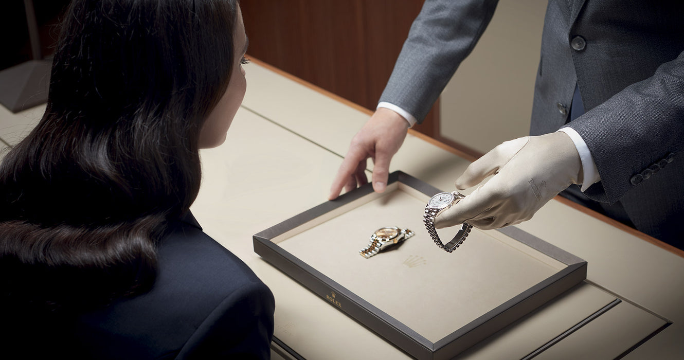 A man in a suit and white glove is presenting a serviced Rolex to a satisfied customer